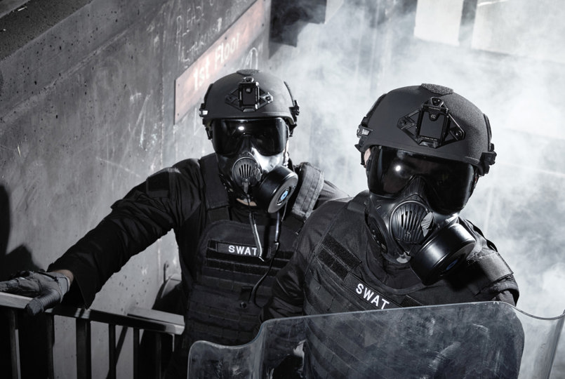 Two soldiers coming up a staircase wearing helmets and respirators with a riot shield
