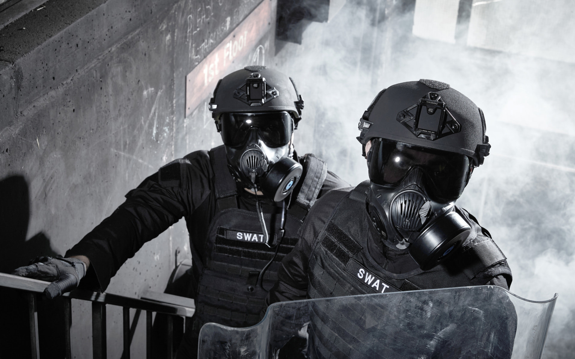 Two soldiers on staircase wearing ballistic helmets and respirators